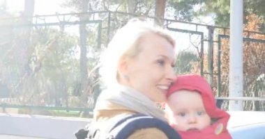Genç, güzel, beyaz bir anne bebeğiyle şehirde yürüyor, gülümsüyor. Mutlu aile zamanları..