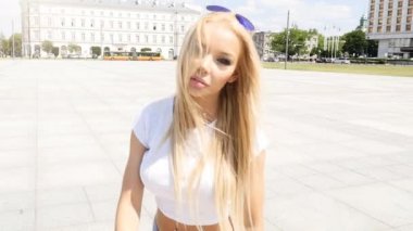 Moda güneş gözlüğü ve kısa kot, güneşli yaz günü şehrin üzerinde yürüyen güzel genç beyaz kız giyiyor.