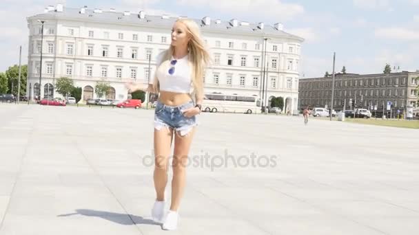 Bella ragazza caucasica che cammina sulla città, indossando occhiali da sole alla moda e jeans corti, giornata estiva soleggiata . — Video Stock