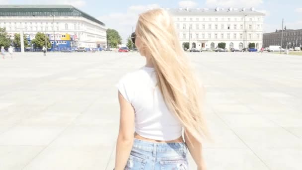 Krásná mladá kavkazské dívka chůzi po městě, nosí módní sluneční brýle a krátké džíny, slunečný letní den. — Stock video