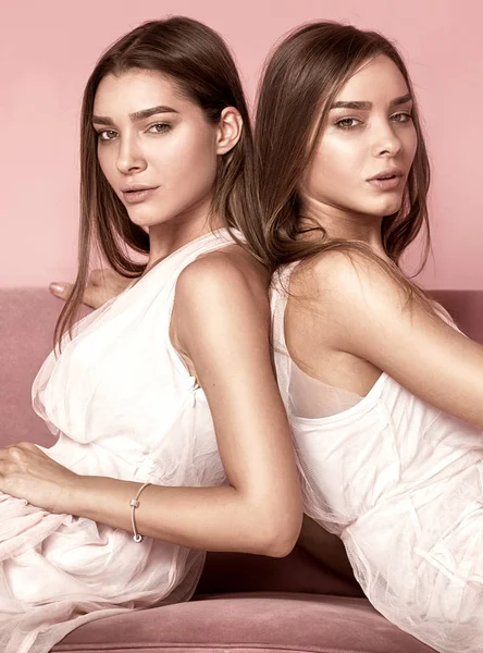 Fashionabla tvillingar systrar poserar på rosa bakgrund. — Stockfoto