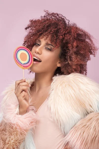 Fashionable afro woman with lollipop on pink background. — Stock Photo, Image