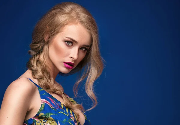 Beautiful blonde young woman with glamour makeup and braid hairstyle posing on blue background.