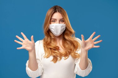 Mavi stüdyo arka planında poz veren tıbbi maske takan genç bir kadının portresi. Virüs konsepti. Sağlığınızı koruyun..