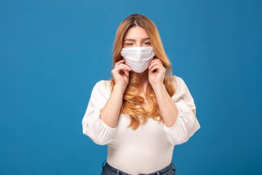 Mavi stüdyo arka planında poz veren tıbbi maske takan genç bir kadının portresi. Virüs konsepti. Sağlığınızı koruyun..