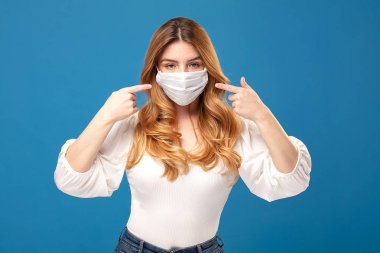 Mavi stüdyo arka planında poz veren tıbbi maske takan genç bir kadının portresi. Virüs konsepti. Sağlığınızı koruyun.. 