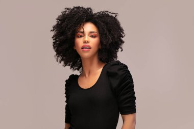 Güzel Afrikalı Amerikalı kadın kameraya bakıyor. Afro saçlı neşeli genç bir kadının portresi. Kıvırcık saçlı güzel kız..