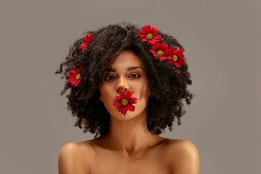 Saçlarında ve dudaklarında güzel çiçekler olan çekici bir afro kadın. Güzellik stüdyosu portresi.