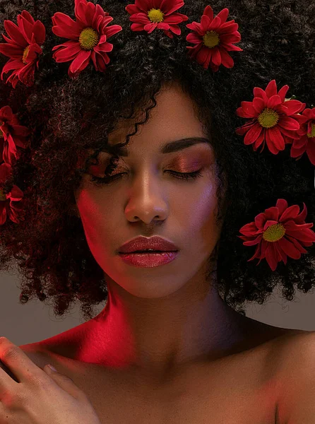 Young attractive afro woman with beautiful flowers in hair. Beauty studio portrait.