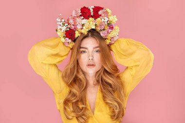 Uzun dalgalı saçlı mutlu bahar bayanının güzel fotoğrafı. Pastel pembe stüdyo arka planında çiçeklerle poz veren kızıl saçlı kız. İnsani duygular, ifade kavramı.