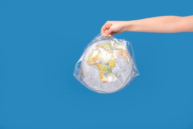 Plastiğe sarılı bir dünya küresi. Plastik kirlilik veya salgın bulaşıcı hastalıklara veya hava kirliliğine karşı koruma. Mavi stüdyo arka planı.