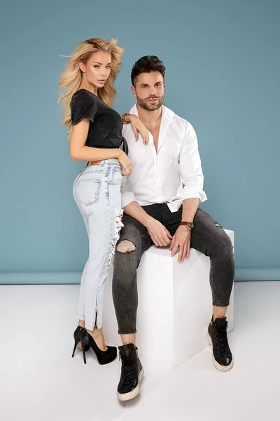 Sensual young couple posing wearing jeans on blue studio background.