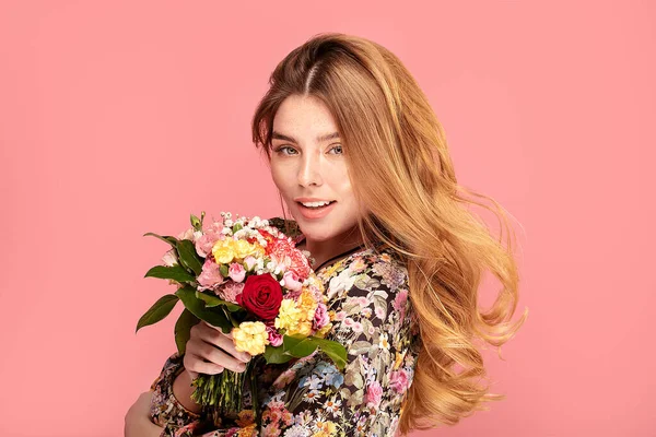 手に花と美の笑顔の女性 ピンクのパステルスタジオの背景に幸せな美しい女の子 春のファッション写真 — ストック写真