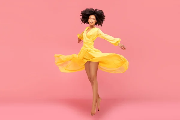 アフロ若いです女性ダンスで黄色マキシドレス上のピンクパステルスタジオ背景 — ストック写真