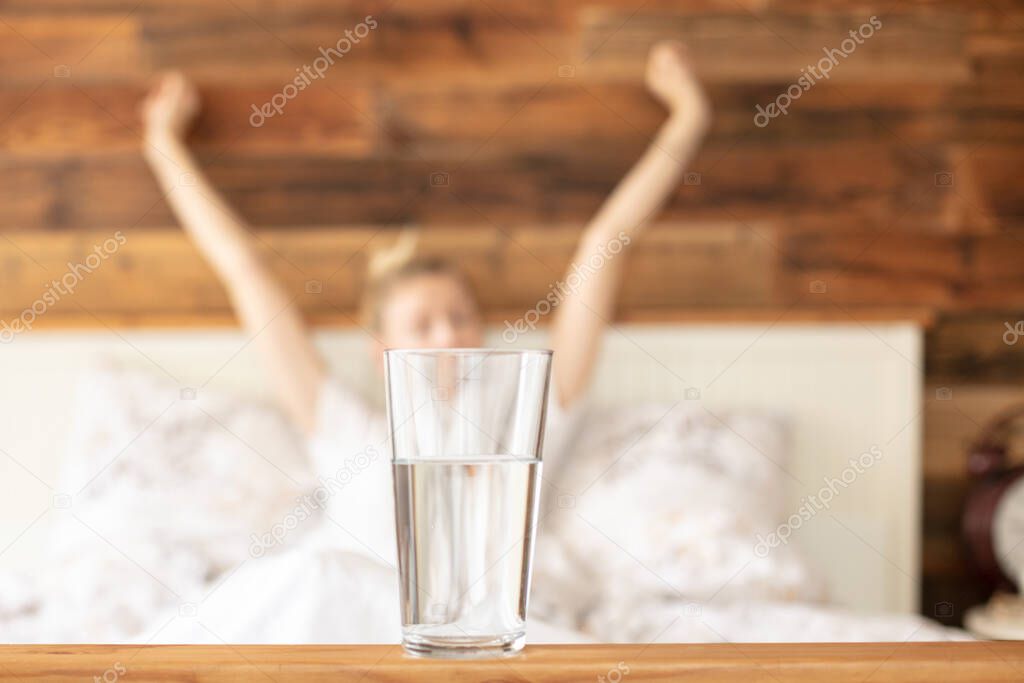 Conceptual photo of glass of water and woman relaxing ,lying in bed at the morning.