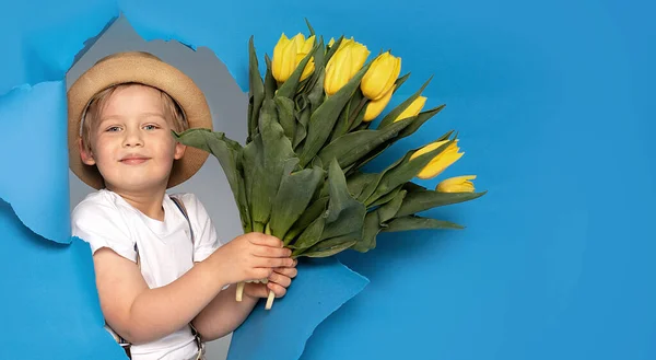 若い白人の子供は青い背景に黄色い花束を持っている 笑顔で幸せな少年 母の日 — ストック写真