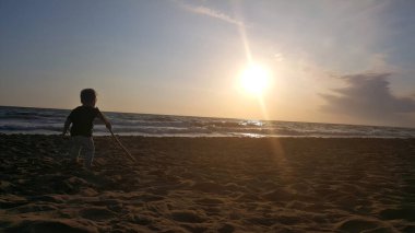 Gün batımında okyanus kumsalında oynayan küçük bir çocuk..