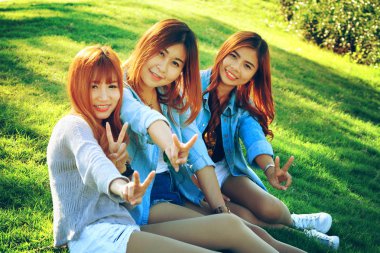 serbest zaman harcama, parkta çimlere oturup, rahatlatıcı üç Asya gülümseme kız
