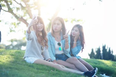 Üç Asyalı kızın selfie 'si boş zamanlarını akıllı telefonlarda geçirir, Chuifong çay bahçesindeki yeşil çimlere oturur, dinlenir.