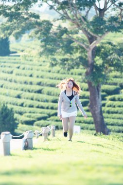 asia woman running on green grass at chuifong tea garden in Chiangrai Thailand clipart