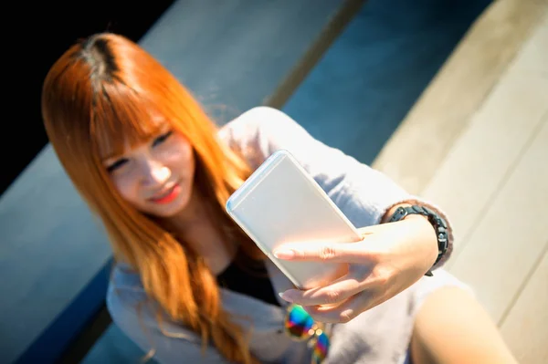 Asiakvinne sitter mot benk og selfie på smarttelefon – stockfoto