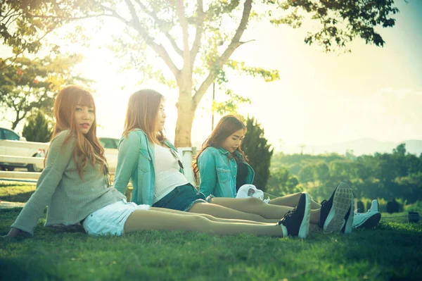 三个亚洲微笑女孩在空闲时间都花 坐在公园的草地上 — 图库照片