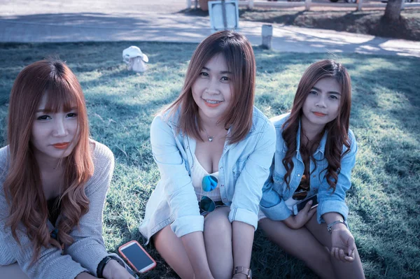 三个亚洲微笑的女孩坐在绿色草地上 — 图库照片