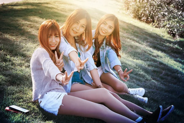 Drie Azië glimlach meisje zitten op groen gras — Stockfoto