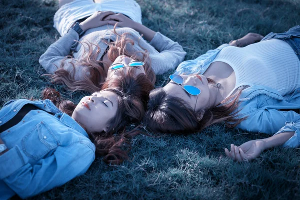 Три азиатские счастливые девушки лежат на зеленой траве в солнечных очках — стоковое фото