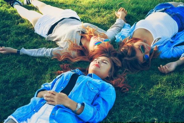 portrait of Three Asia happy girls lying on green grass in sunglasses