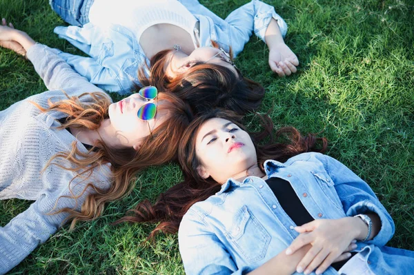 Три азиатские счастливые девушки лежат на зеленой траве в солнечных очках — стоковое фото