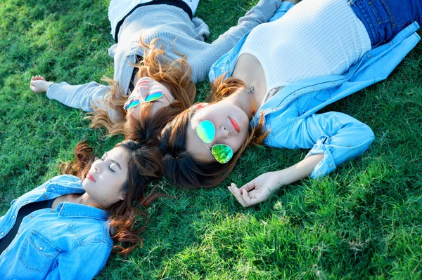Three Asia happy girls lying on green grass in sunglasses