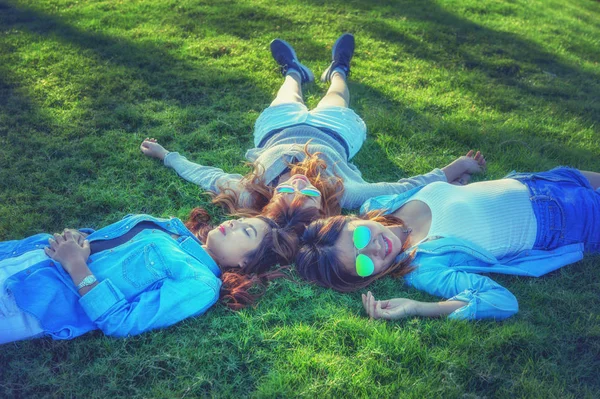 Three Asia happy girls lying on green grass in sunglasses