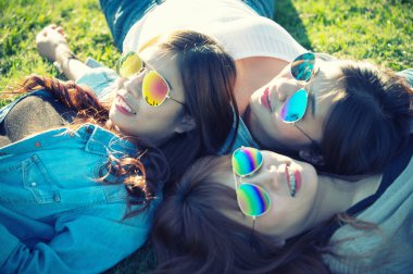 Üç Asya mutlu kız güneş gözlüğü yeşil çim üzerinde yalan