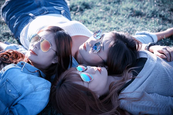 Three Asia happy girls lying on green grass in sunglasses