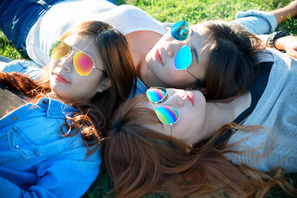 Drei asiatische glückliche Mädchen liegen mit Sonnenbrille auf grünem Gras — Stockfoto