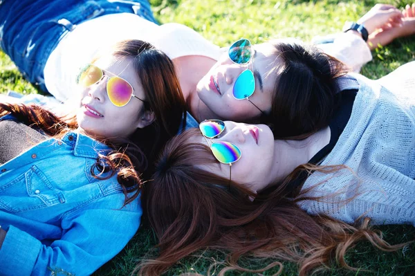 Three Asia happy girls lying on green grass in sunglasses