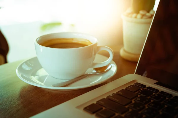 Filiżanka kawy i laptop na drewnianym stole — Zdjęcie stockowe