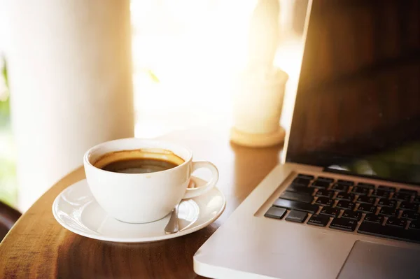 Filiżanka kawy i laptop na drewnianym stole — Zdjęcie stockowe