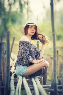 Off Shoulder tişörtlü ve kısa pantolonlu Asyalı bir kadın doğada oturuyor.
