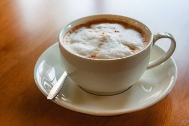 Ahşap masa üzerinde sıcak cappuccino Kupası.
