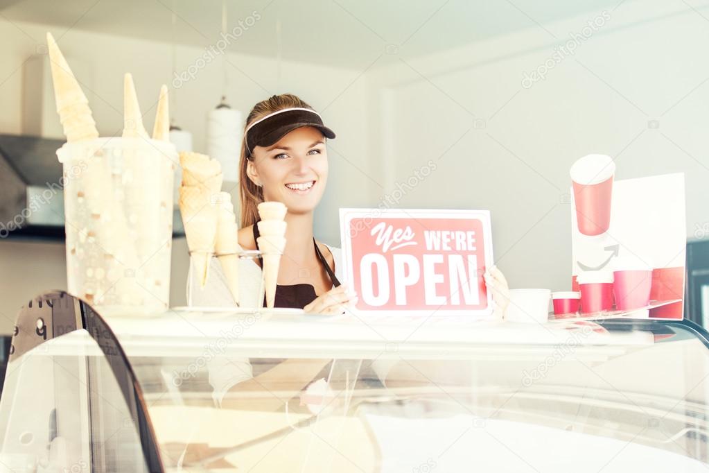 Young woman holding OPEN sign. Coffee and Ice-cream store. 