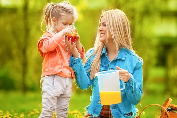 Мать и дочь пьют апельсиновый сок в парке — стоковое фото