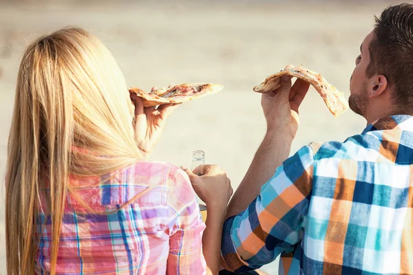 Láska pár jíst pizzu a popíjeli pivo na pláži — Stock fotografie