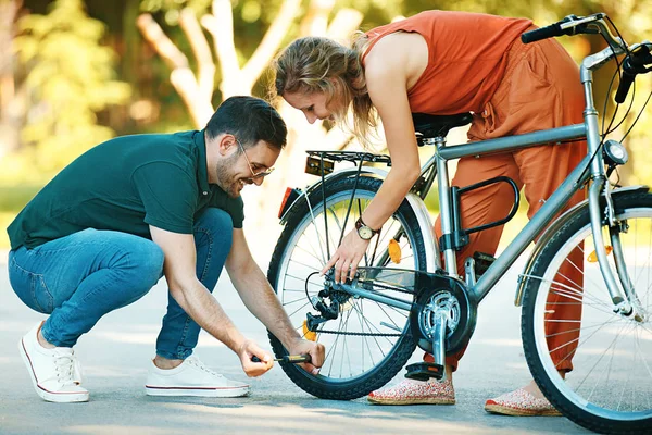 Jovem ajudando a mulher com sua bicicleta . — Fotografia de Stock