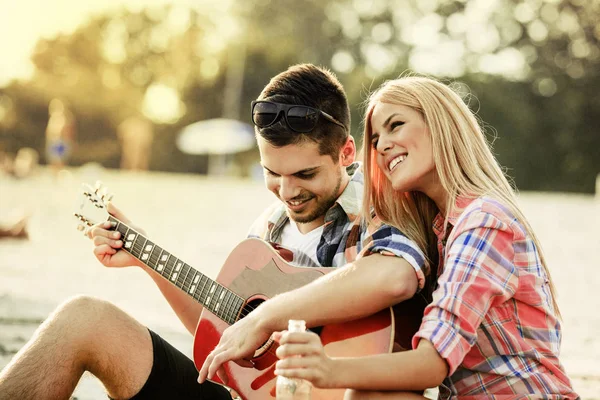Молодой человек играет на гитаре со своей девушкой — стоковое фото