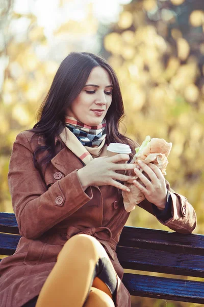 Sandviç ve sıcak bir içecek olan parkta güzel kadın