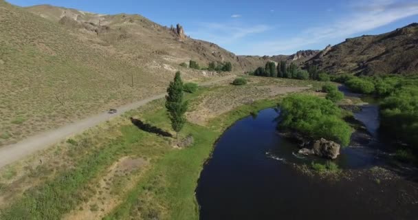 Drohnen-Szene einer Schotterroute mit einem Auto, das verfolgt wird, und einem Fliegenfischer in einem Steppen-Szenario in Südpatagonien, Argentinien. Kamera, die sich auf einer Straßenseite vorwärts bewegt. einem Lieferwagen folgend. — Stockvideo