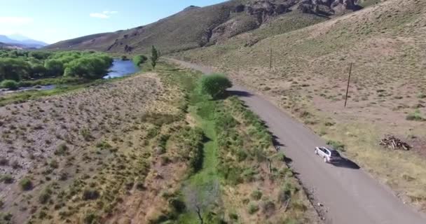 Drohnen-Szene einer Schotterstraße in einem Steppenortungswagen, der sich vorwärts bewegt. Berge im Hintergrund. Wüste ländliche Landschaft mit Fliegenfischen Fluss auf der linken Seite. — Stockvideo