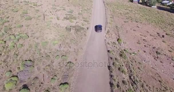 Escena aérea, la cámara se mueve de la vista superior a la perspectiva. Van y coche pasa a través de la carretera de grava en un paisaje de estepa. Sandy, zona seca. Patagonia, Argentina . — Vídeo de stock